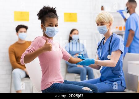 Felice vaccinato ragazza gesturante Thumbs-Up dopo il vaccino Covid-19 in ospedale Foto Stock