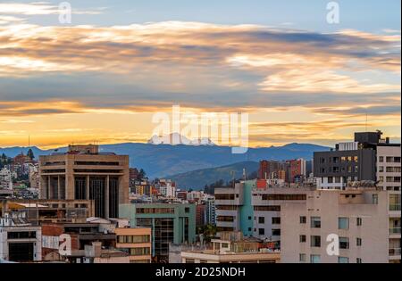 Paesaggio urbano aereo a lunga esposizione di Quito con edifici di appartamenti e il vulcano Antisana innevato all'alba, Ecuador. Foto Stock