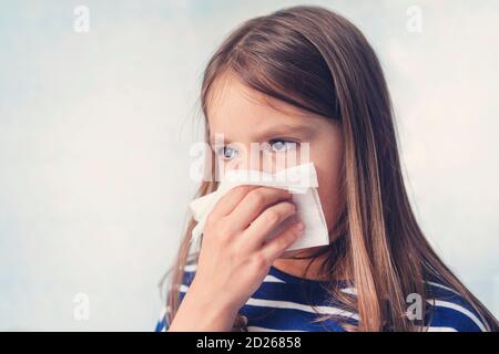 bambina con fazzoletto. Una ragazza fredda soffia il naso in un panno bianco su uno sfondo blu. Malattie e raffreddori. Rinite non runny naso chiuso Foto Stock