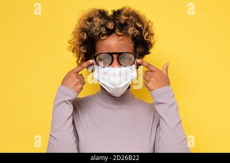 Donna afroamericana con occhiali foggy causato da indossare un Maschera protettiva COVID Foto Stock