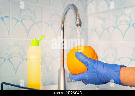 La persona lava la frutta con sapone ecologico per il lavaggio in una cucina con pareti blu. Decontaminazione e disinfezione dei prodotti dal punto vendita. Prevenzione di Foto Stock