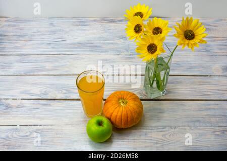 Succo di mela di zucca in vetro su tavolo di legno. Fiori gialli, zucca e mela accanto al succo. Concetto di cibo sano. Messa a fuoco selettiva. Foto Stock