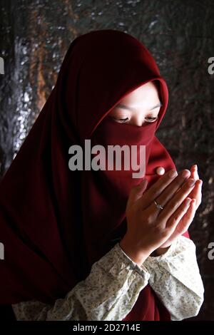 Un ritratto di una donna asiatica velata che prega in modo islamico. Bel modello musulmano che indossa abiti rossi Foto Stock