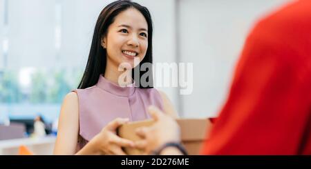 Donna d'affari asiatica felice che prende le scatole della pizza dall'uomo di consegna della pizza, pausa pranzo, consegna della pizza del take-away, cibo e bevanda Foto Stock