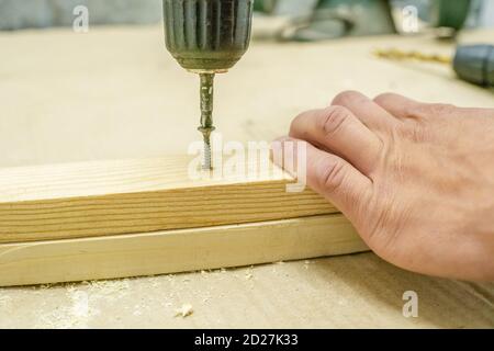 Le mani maschio avvitano i blocchi di legno sulle tavole con un cacciavite Foto Stock