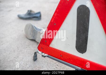 Un incidente sulla strada che coinvolge una persona. Primo piano dello stivale di un uomo e un segnale di arresto di emergenza triangolo rosso Foto Stock
