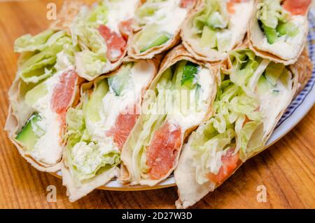 Tortilla arrotola con salmone, formaggio tenero, lattuga e cetriolo fresco primo piano su un piatto Foto Stock