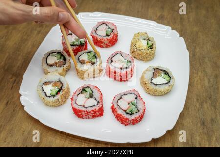 Vari sushi giapponesi su piatto bianco con bastoncini di legno sfondo Foto Stock