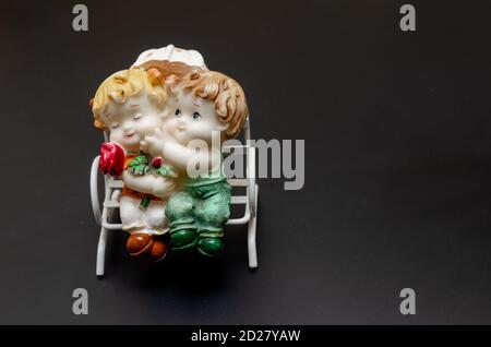 Figurine in ceramica di bambini su una panchina su un nero sfondo Foto Stock