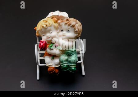Figurine in ceramica di bambini su una panchina su un nero sfondo Foto Stock