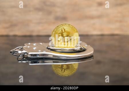 Moneta di bitcoin d'oro con polsini a mano sullo sfondo di legno con riflessione Foto Stock