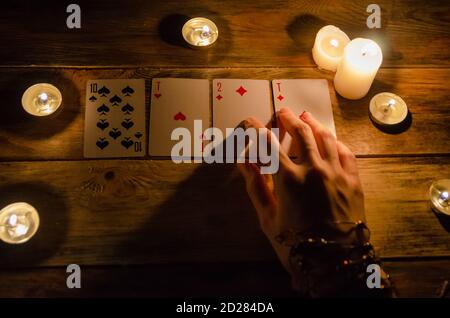 Mani di un teller di fortuna e carte sul tavolo, intorno a candele illuminate nel buio su un tavolo di legno. Concetto di divinazione, magia. Vista in alto Foto Stock