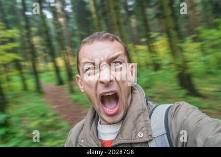 uomo di bruna urlando nella foresta con voce spaventata, ritratto di un uomo urlante con la sua bocca aperta nella foresta autunnale Foto Stock