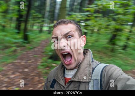 uomo di bruna urlando nella foresta con voce spaventata, ritratto di un uomo urlante con la sua bocca aperta nella foresta autunnale Foto Stock