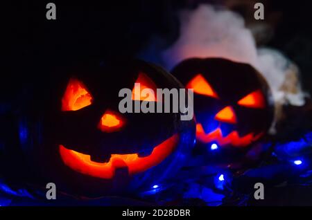 Due zucche incandescenti al buio nel fumo nei primi passi della foresta. Una zucca si sbirca da dietro l'altra. Splendido sfondo per Halloween. Foto Stock