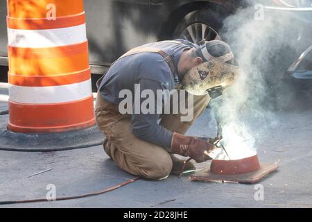 Lavoratore di saldatura piastra di acciaio sulla strada, NYC Foto Stock