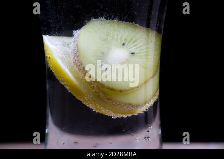 Sfondo di limoni, fette di kiwi in acqua con bolle dietro il vetro Foto Stock