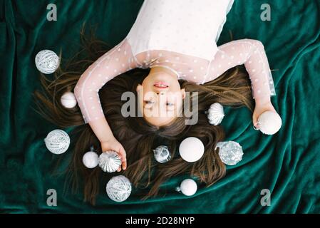 Ragazza sdraiata sul pavimento su una coperta, palline bianche di Natale, accanto all'albero di Natale, vista dall'alto, concetto di nuovo anno Foto Stock