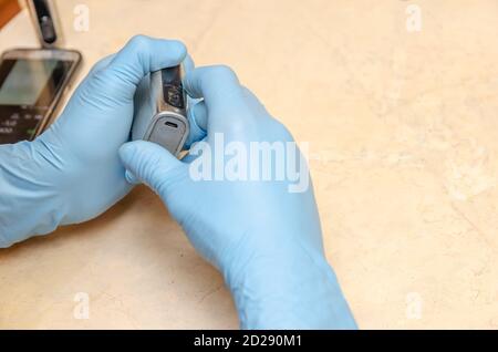 Le mani maschili in guanti blu riparano una sigaretta elettronica su un tavolo luminoso in legno da vicino Foto Stock