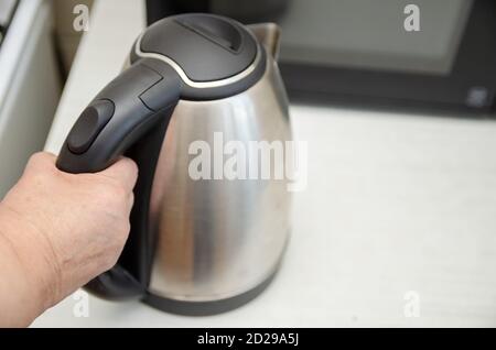 Mano di una donna anziana che tiene un bollitore elettrico primo piano, copia spazio Foto Stock