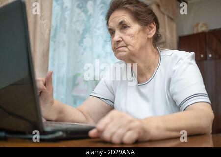 La donna anziana dai capelli scuri è seduta ad una scrivania che sta scrivendo sopra un computer portatile Foto Stock
