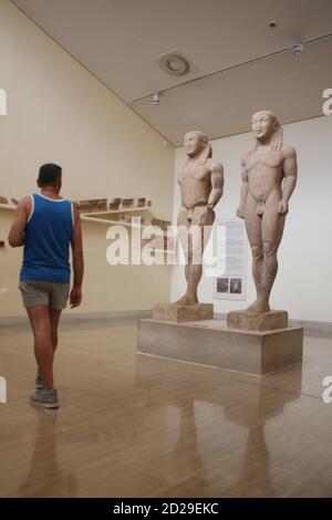 Un uomo che cammina tra Cleobis e Biton, i giganti Kouroi di Delfi nel museo archeologico del sito in Grecia Foto Stock