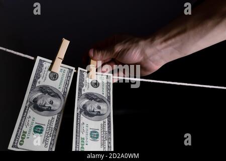 la mano dell'uomo appende i dollari su uno sfondo nero usando i clothespins su un concetto di corda. di soldi sporchi. Foto Stock