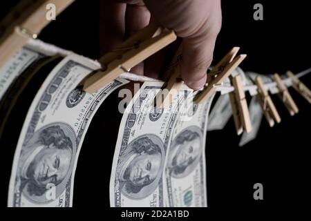 la mano dell'uomo appende i dollari su uno sfondo nero usando i clothespins su un concetto di corda. di soldi sporchi. Foto Stock