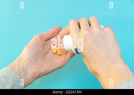 Una mano versa le capsule di vitamina gialla nell'altra mano su sfondo blu Foto Stock