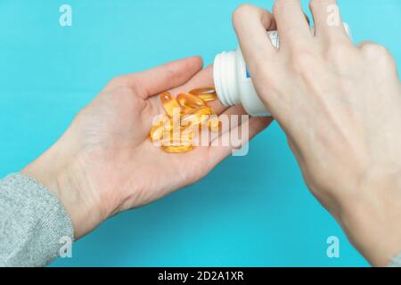 Una mano versa le capsule di vitamina gialla nell'altra mano su sfondo blu Foto Stock