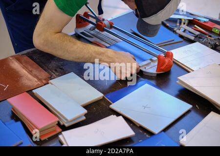 Le mani degli uomini tagliano le piastrelle sul tavolo usando un manuale taglierina Foto Stock