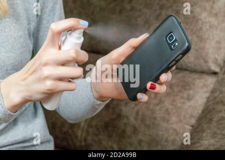 Le mani delle donne disinfettano un telefono cellulare nero con un aerosol antisettico Foto Stock