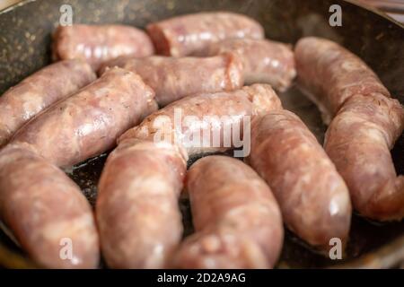 Le salsicce crude vengono fritte in una padella ravvicinata Foto Stock