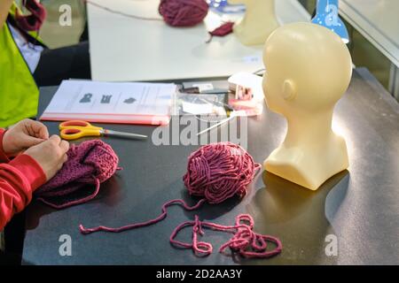 Le mani delle donne hanno lavorato a maglia un cappello dai fili di lana con l'aiuto di Spokes. Un'azienda con prodotti di lana fatti a mano. Foto Stock