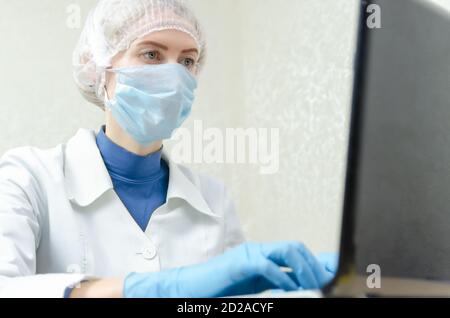medico in un abito medico, guanti medici blu sta lavorando a un computer portatile, accanto a uno stetoscopio. Concetto di medicina Foto Stock