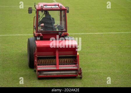 Un uomo in un trattore con seminatrice a disco affossare l'erba su un campo di calcio Foto Stock