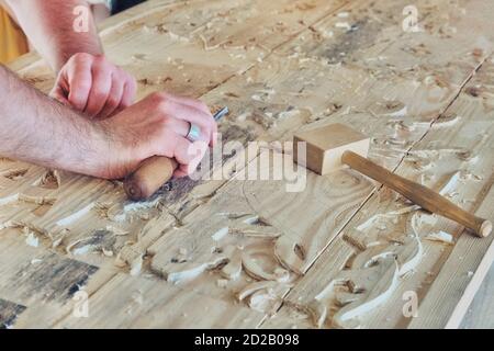 Le mani del padrone tagliano un modello su una grande tavola di legno. Creazione di modelli scolpiti per mobili e articoli per la casa. Lavori sul progetto nella carpenta Foto Stock