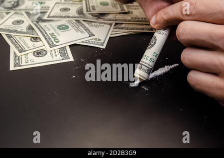 Mani maschili che sniffing le droghe attraverso un dollaro su un nero primo piano sullo sfondo Foto Stock