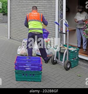 Tesco alimentari shopping in borsa di plastica consegna furgone driver & borse alla porta anteriore mantiene la distanza sociale che il cliente indossa Maschera facciale Covid 19 UK Foto Stock