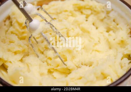 Primo piano la mano della donna che fa purè di patate con miscelatore in pentola. Cottura di purè di patate. Foto Stock