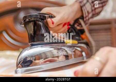 Primo piano di una mano di donna con chiodo rosso polacco con un ferro vecchio che ferri una t-shirt a righe Foto Stock