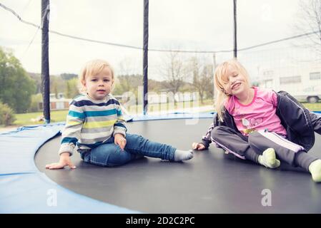 Due bei bambini seduti sul trampolino e in posa. Tempo di riposo e preparazione per il salto. Foto Stock