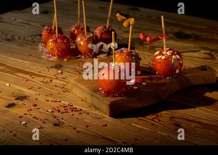 Mele in caramello rosso, decorate con decorazioni su una tavola di legno su sfondo scuro. Concetto di cibo festivo. Foto Stock