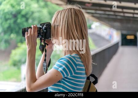 Bionda ragazza scatta foto sulla macchina fotografica sul ponte in tempo soleggiato Foto Stock