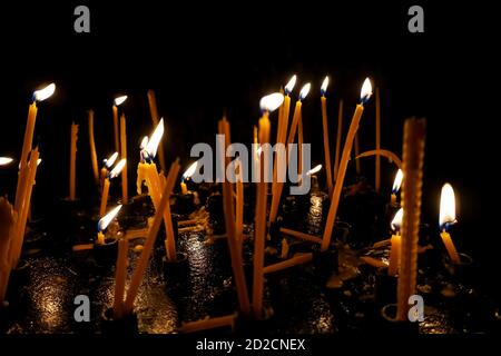 Molte candele bruciano nella chiesa al buio. Un gruppo di candele che bruciano al buio con una profondità di campo poco profonda. Primo piano. Foto Stock