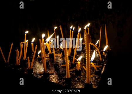 Molte candele bruciano nella chiesa al buio. Un gruppo di candele che bruciano al buio con una profondità di campo poco profonda. Primo piano. Foto Stock