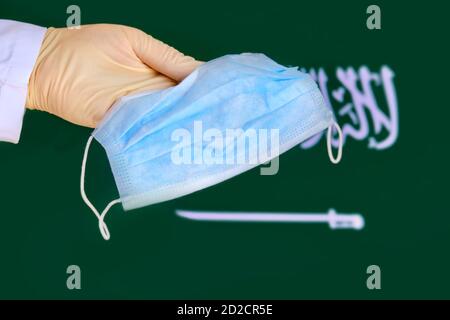 Indossate un guanto protettivo con una maschera medica sullo sfondo della bandiera dell'Arabia Saudita, l'epidemia di coronavirus Concept. Il medico tiene una maschera di viso agai Foto Stock