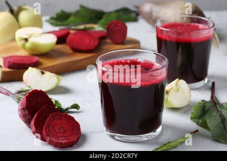 Due bicchieri di succo fresco con barbabietole e mele. Barbabietole e mele tritate su tavola grigia. Primo piano. Formato orizzontale Foto Stock