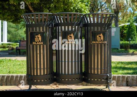 Moderni contenitori in metallo per la raccolta differenziata dei rifiuti nel parco in una giornata di sole da vicino. Traduzione: 'Plastica, vetro, carta.' Foto Stock