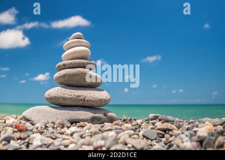 Piramide di ciottoli sulla spiaggia su uno sfondo di cielo blu con nuvole in una giornata di sole. Il concetto di armonia di equilibrio e meditazione. Copia spazio Foto Stock